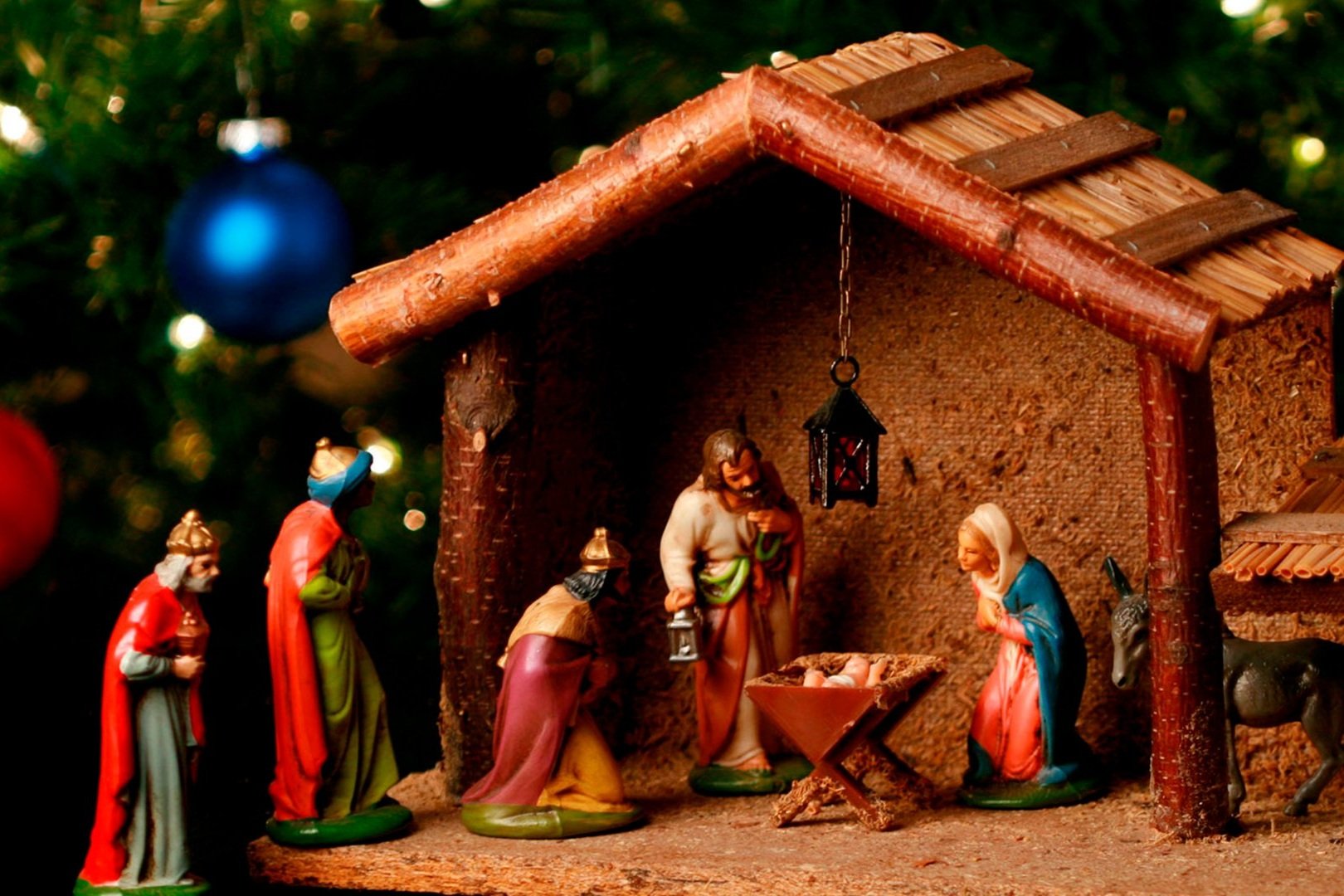 Presépio de figuras em um estábulo de madeira, ao lado de uma árvore de Natal