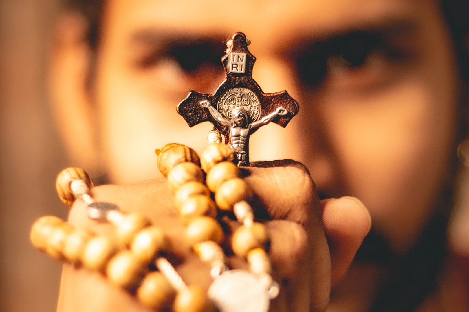 Homem segurando um terço com crucifixo diante do rosto