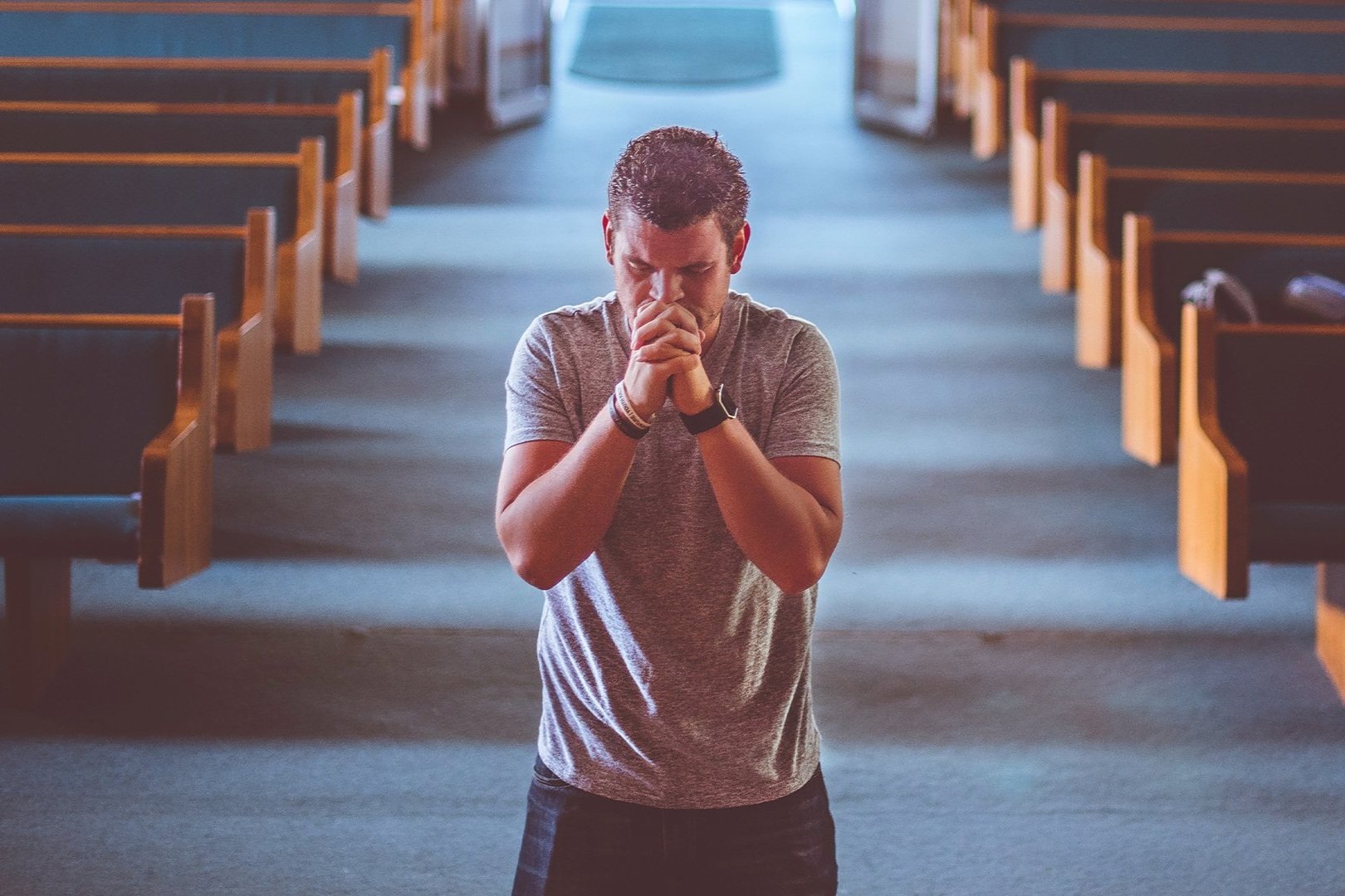 Homem de mãos postas rezando, sentado em um banco de igreja