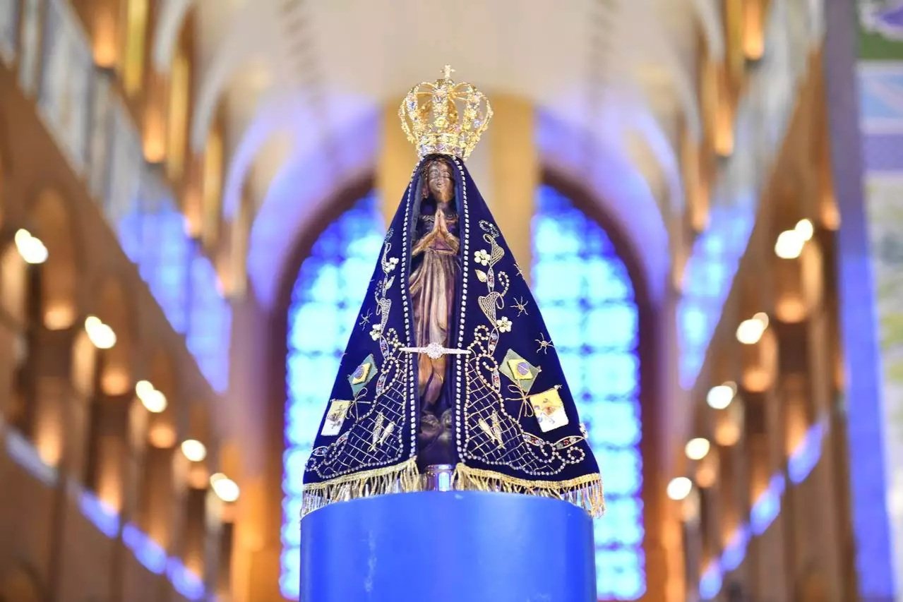 Imagem de Nossa Senhora Aparecida iluminada, no interior da basílica com vitrais azuis