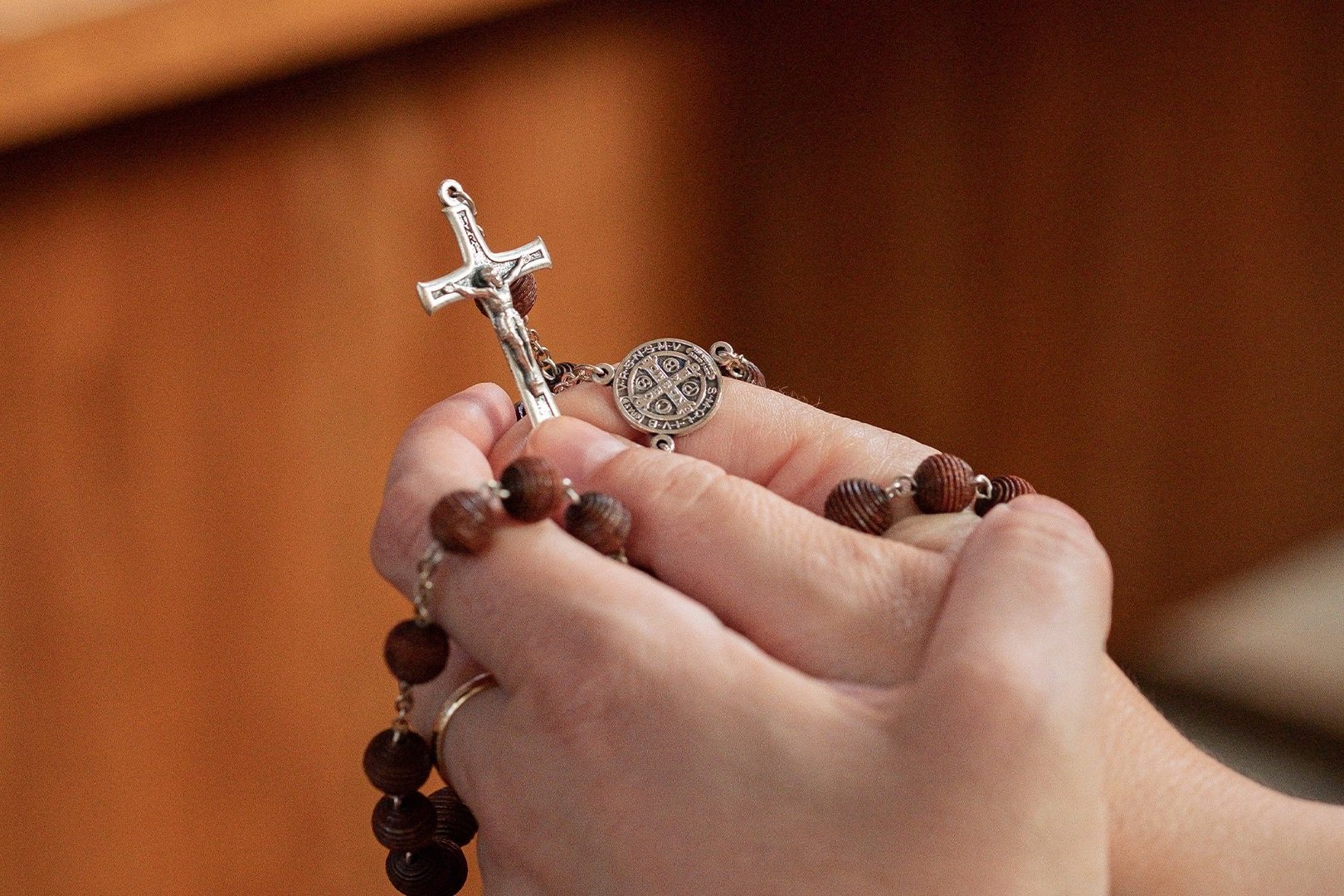 Mãos unidas segurando um terço com crucifixo prateado
