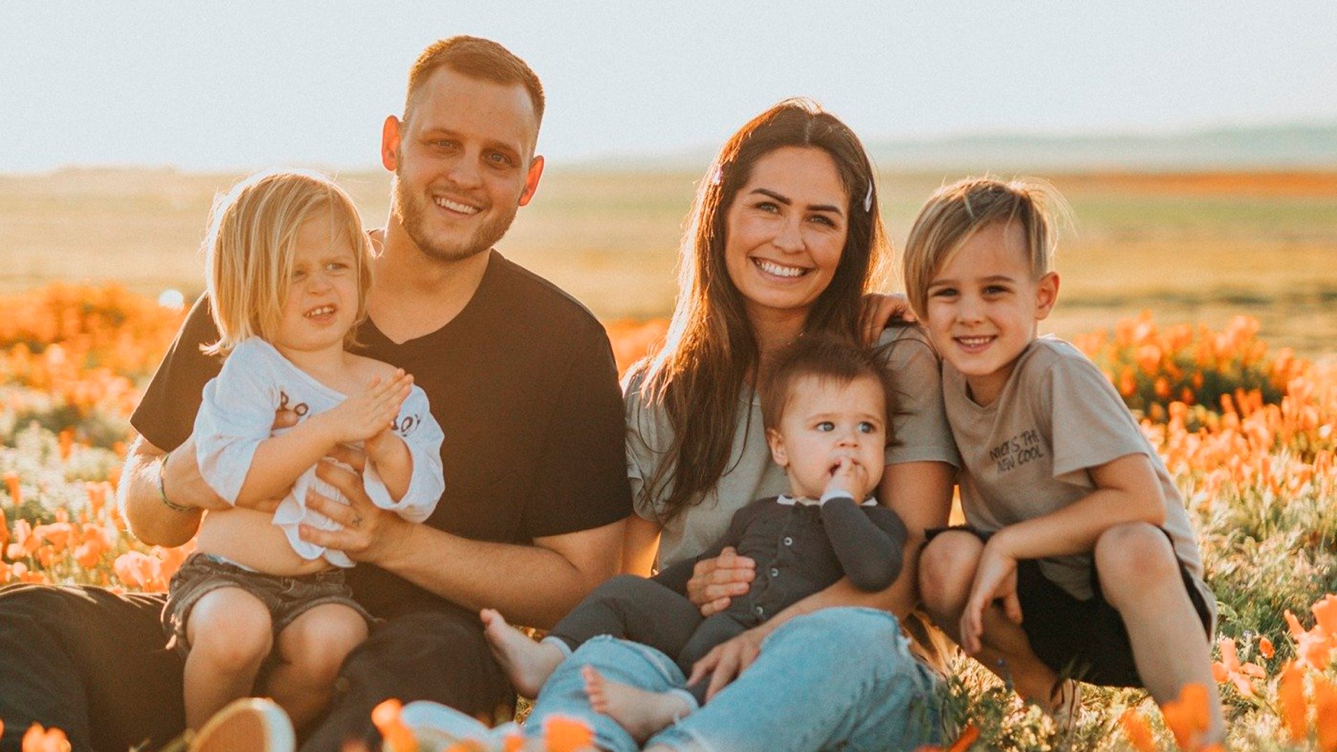 Família sorridente sentada em um campo florido, com três filhos pequenos