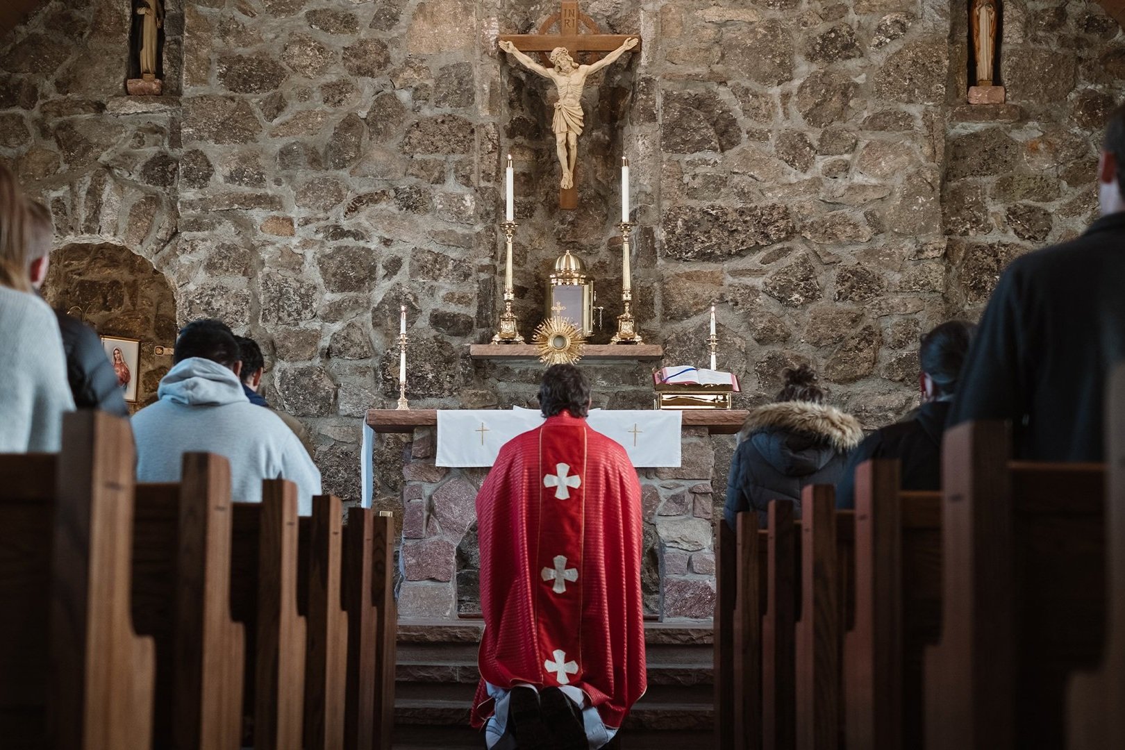 Fiéis sentados nos bancos de uma igreja de pedra, vistos por trás