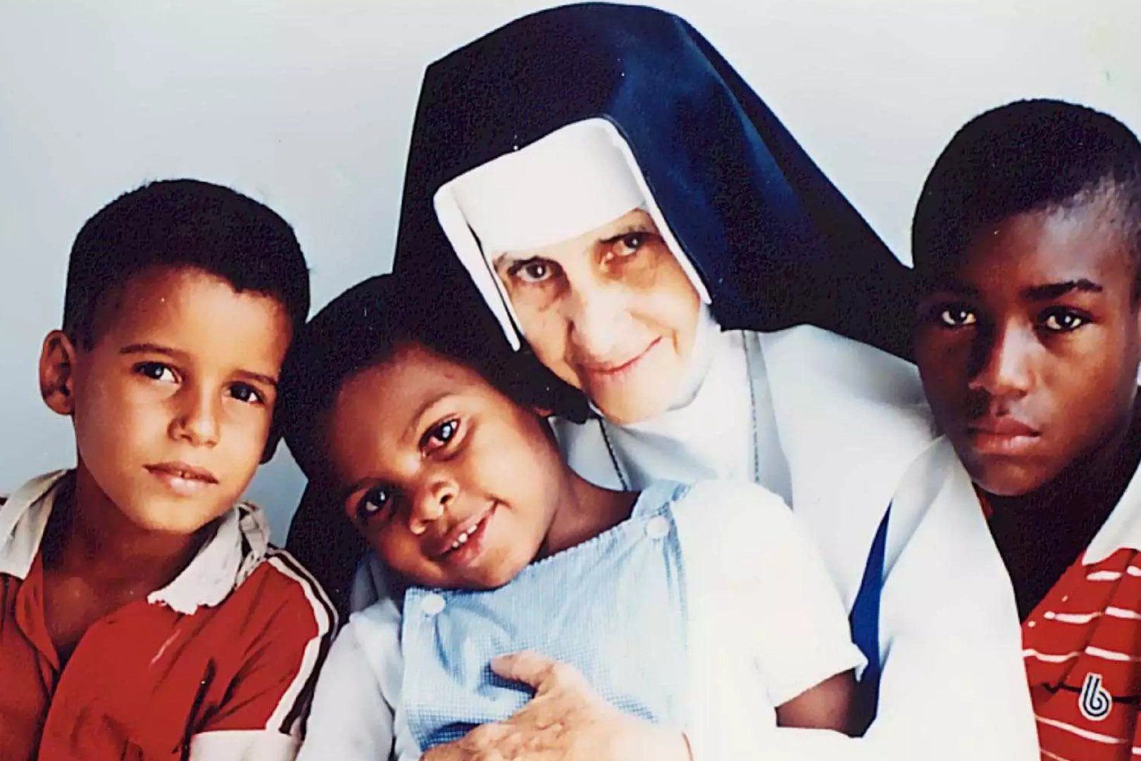 Santa Dulce dos Pobres, de hábito e véu, abraçando três crianças