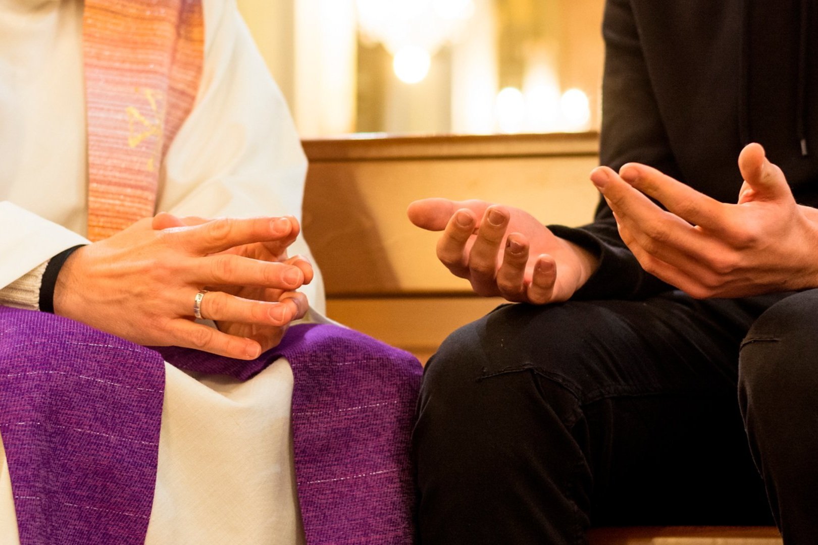 Mãos de um sacerdote de estola roxa diante de um fiel, durante a confissão
