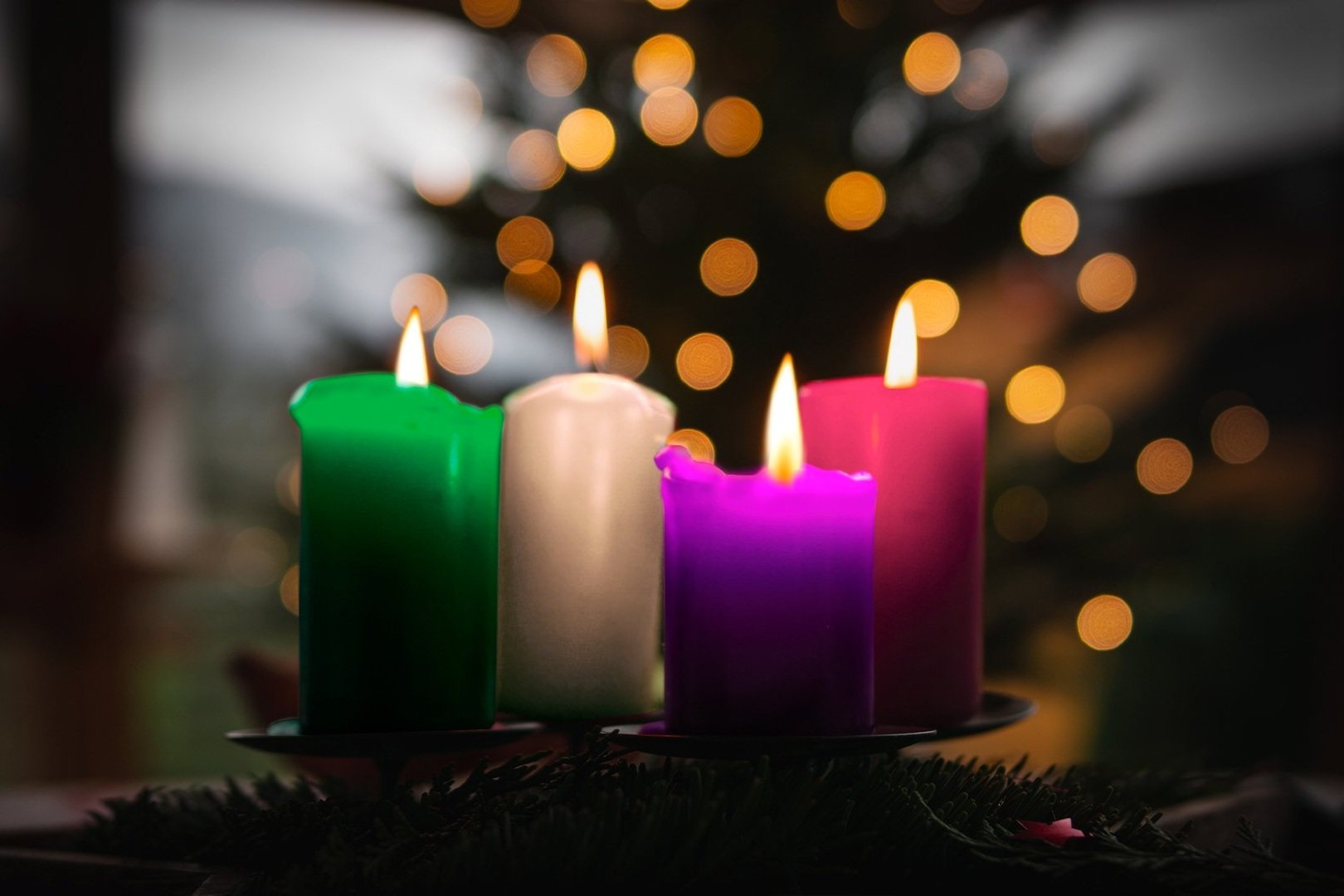 Coroa do Advento com quatro velas coloridas acesas, sobre fundo de luzes