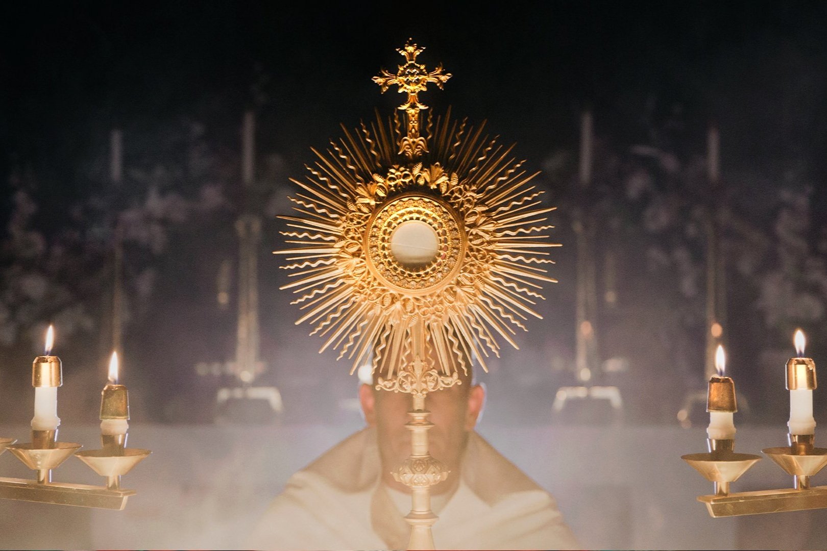 Ostensório dourado com a hóstia consagrada, entre velas acesas