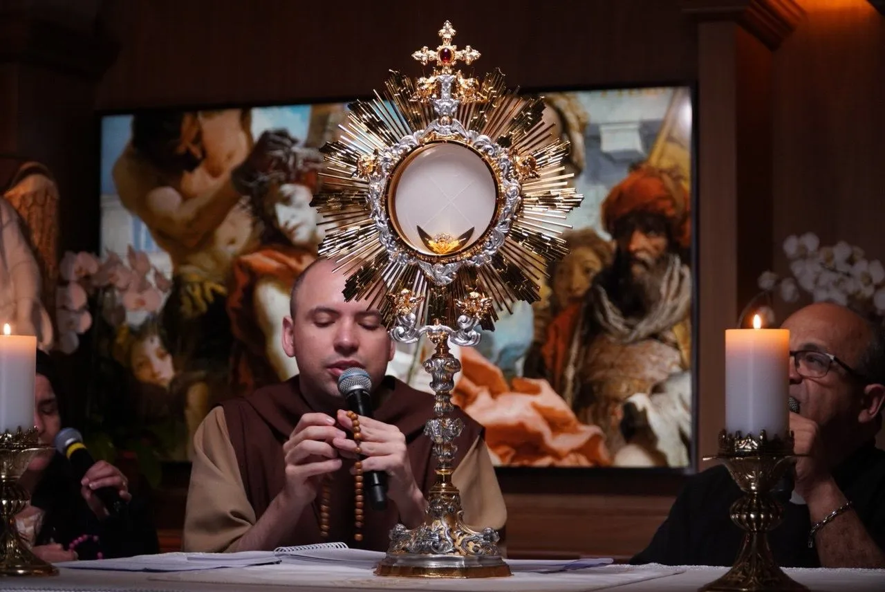 Fiéis em adoração ao Santíssimo, diante de um ostensório e velas acesas